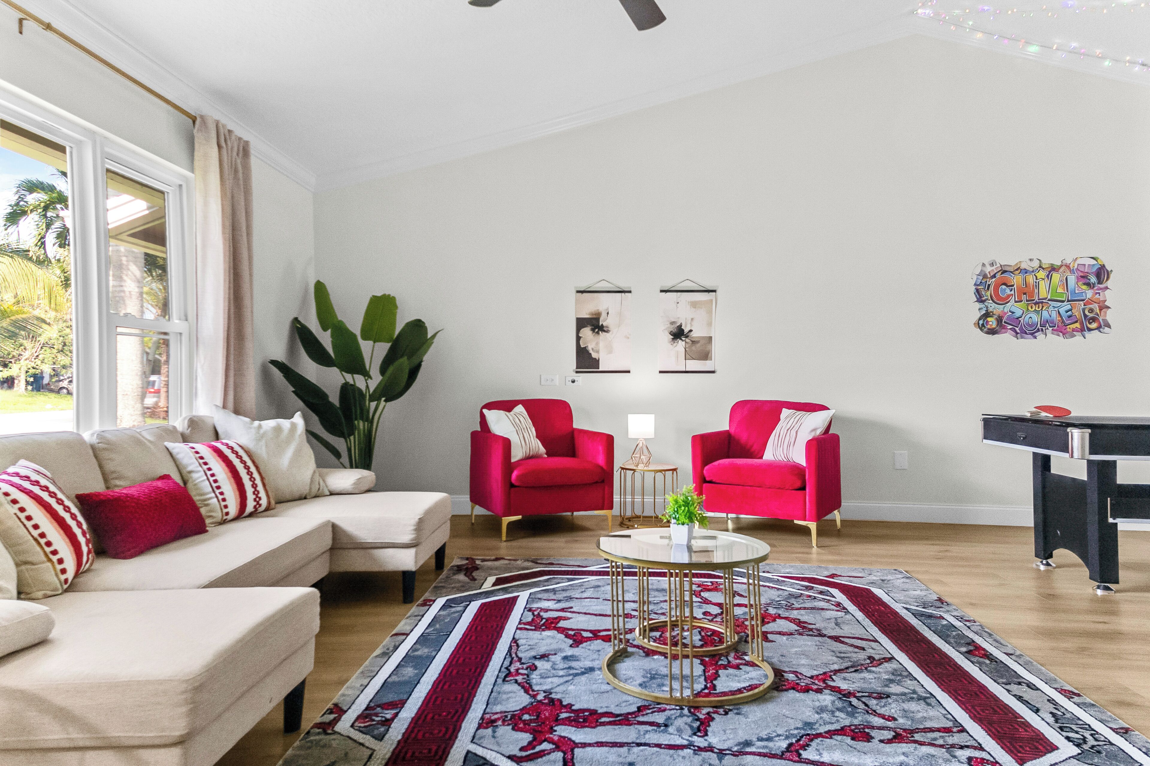 Ein Wohnzimmer mit einem beigen Sofa, zwei roten Sesseln, einem Couchtisch und einem gemusterten Teppich.