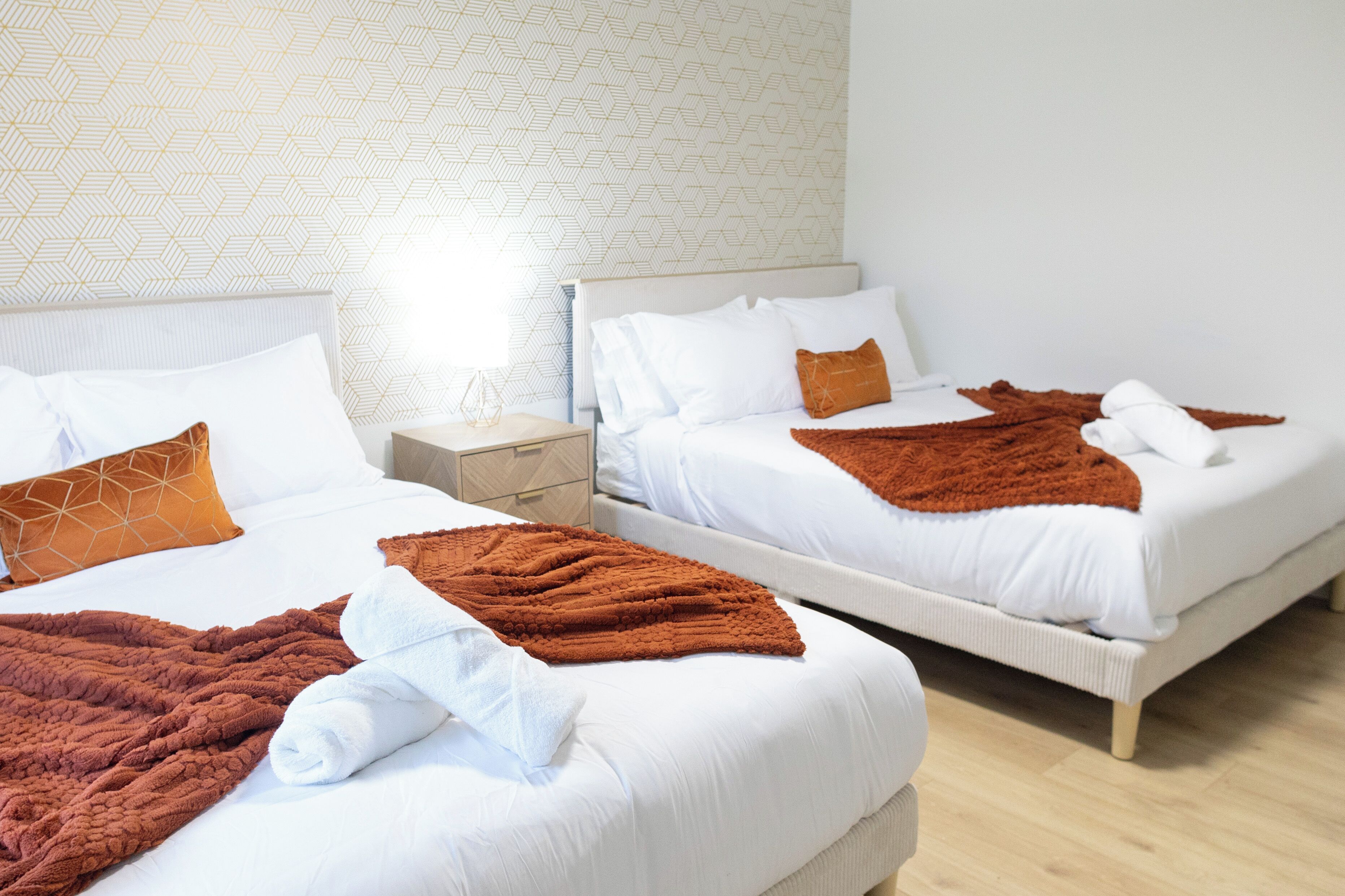 Two beds with white bedding, brown throw blankets, and a geometric patterned wall.
