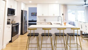 A modern kitchen with white cabinets, stainless steel appliances, and a bar area with stools.
