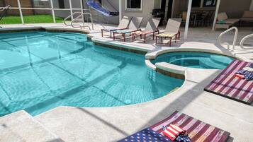 A swimming pool with lounge chairs and a hot tub.