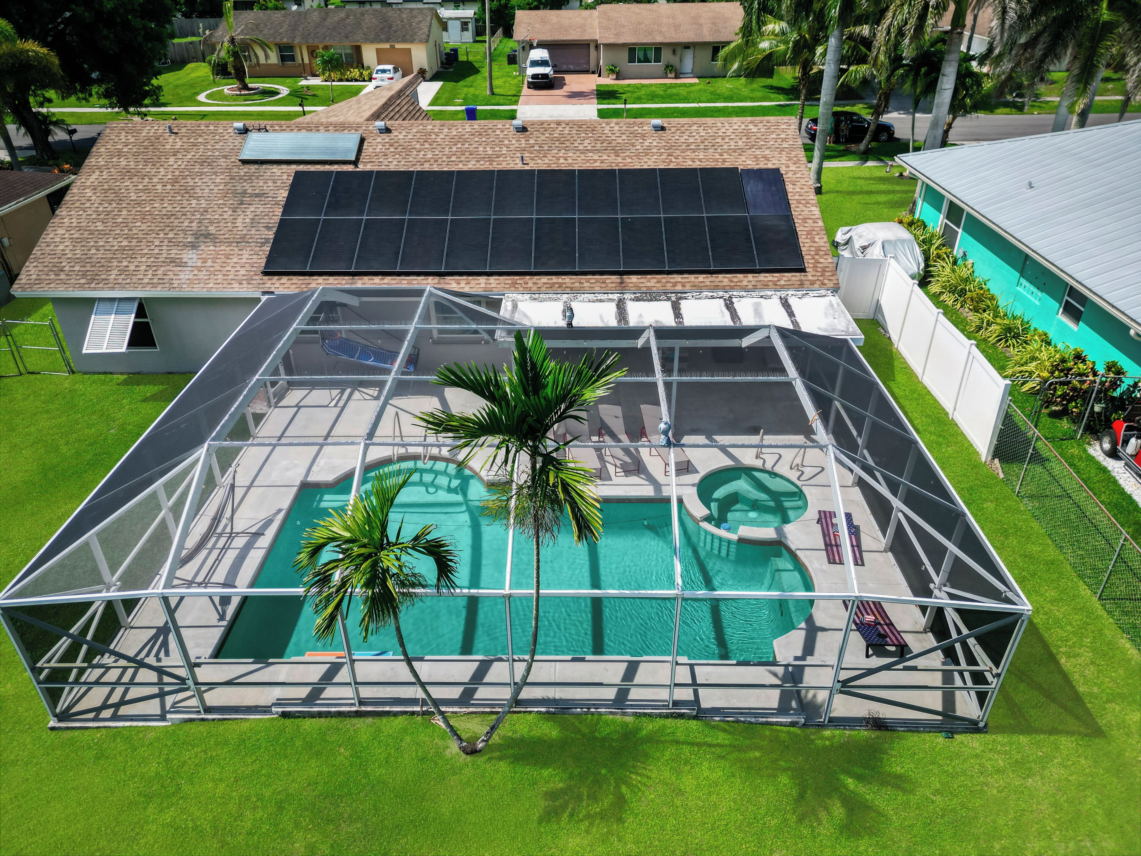 A residential property with a covered swimming pool, solar panels, and a fenced yard.