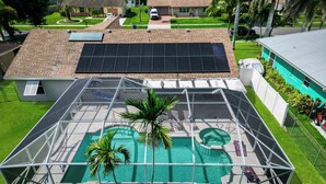 A residential property with a covered swimming pool, solar panels, and a fenced yard.