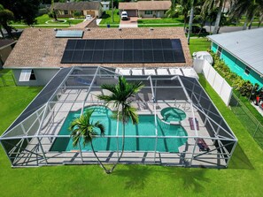 A residential property with a covered swimming pool, solar panels, and a fenced yard.