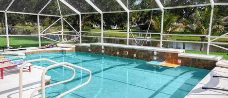 A swimming pool with a safety fence, lounge chairs, and a hot tub area.