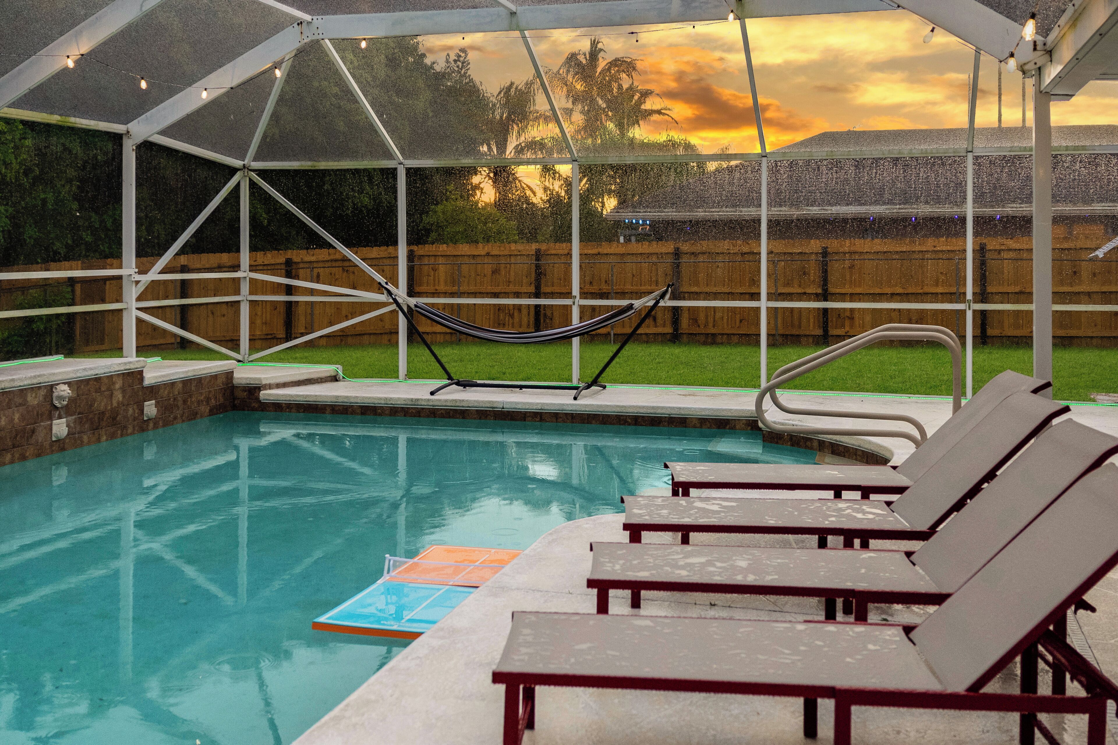 An outdoor swimming pool with a hammock, lounge chairs, and a covered area with string lights.
