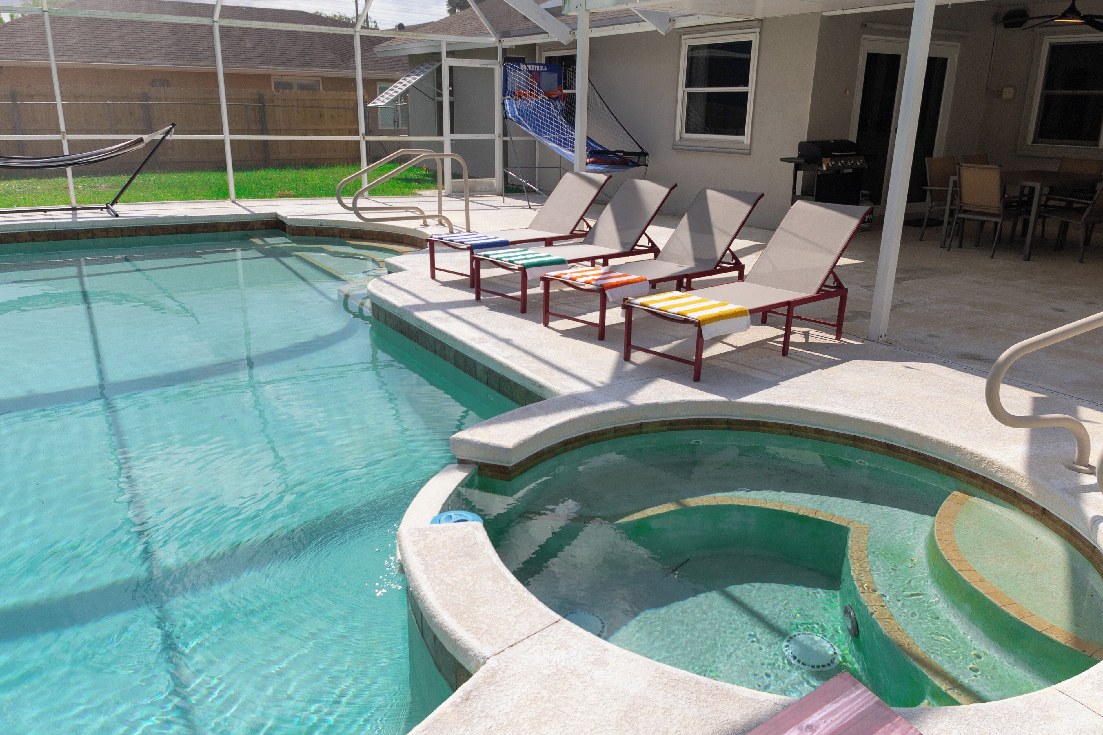 A swimming pool with a sun deck area, lounge chairs, and a basketball court.
