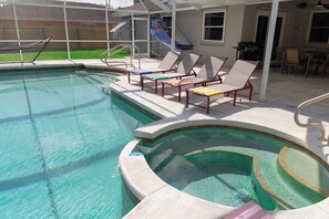 Una piscina con solárium, sillas de descanso y una cancha de baloncesto.