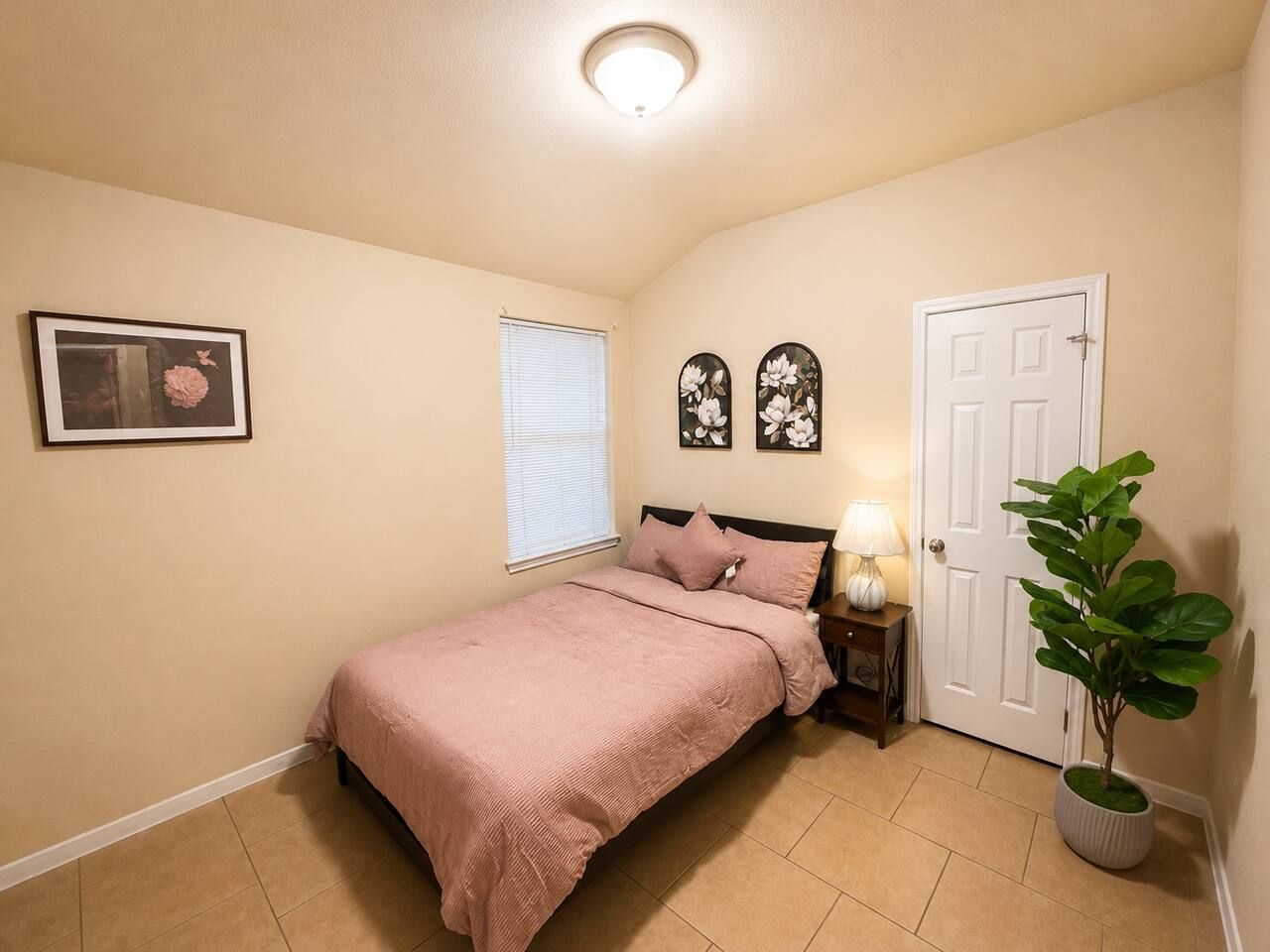 Une chambre à coucher avec un lit, une table de chevet, une lampe, une porte et une plante en pot.