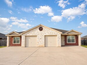 A residential house with a stone facade, two garage doors, and a clear sky. - 3BR Near Fort Cavazos | TDY • PCS • Extended Stay (Killeen)