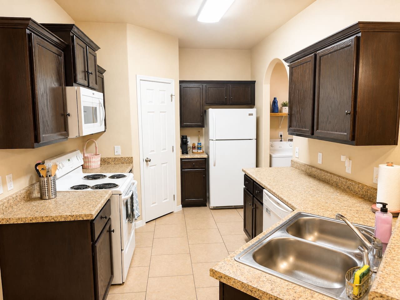A compact kitchen with dark wooden cabinets, a white refrigerator, a stove, and a sink.