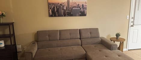 A sectional sofa in a living room with a cityscape painting above it.