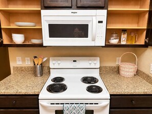 A kitchen with a white microwave, stove, and granite countertop. There are wooden cabinets above and below the counter. - 3BR Near Fort Cavazos | TDY • PCS • Extended Stay (Killeen)