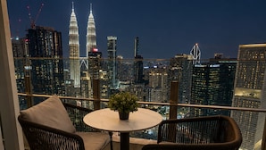 Ein Balkon mit Blick auf die Skyline der Stadt, darunter die Petronas Towers, mit zwei Korbstühlen, einem kleinen Tisch und einem Blumentopf.