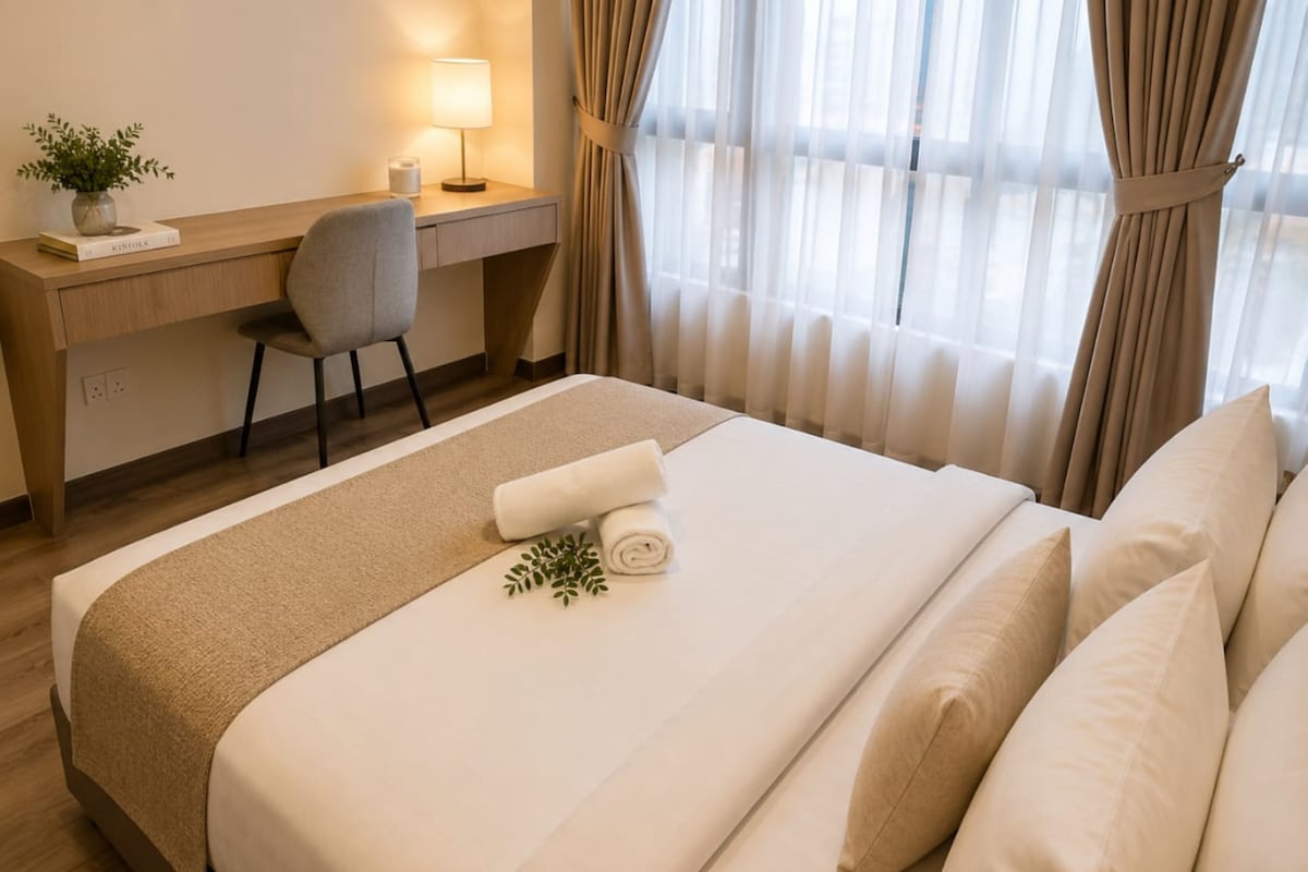 Et hotelværelse med seng, skrivebord, stol, lampe og et vindue med gardiner.