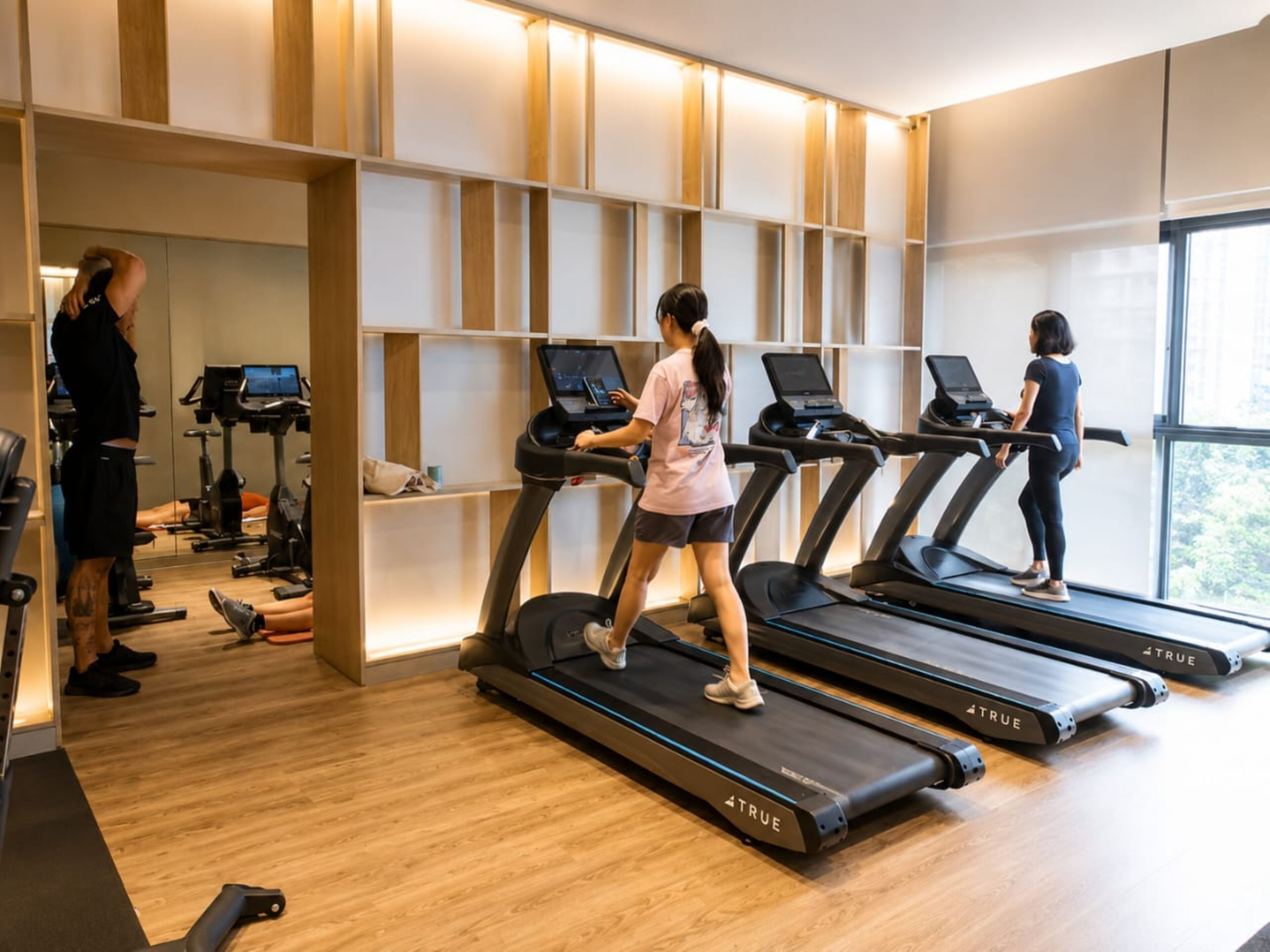 Un gimnasio con cintas de correr, equipo de ejercicio y un amplio ventanal que proporciona luz natural.