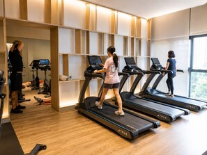 Et fitnesscenter med løbebånd, træningsudstyr og et stort vindue, der giver naturligt lys.