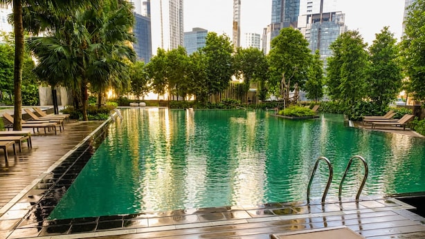 Ein Swimmingpool mit Stadtansicht im Hintergrund, umgeben von Palmen und Liegestühlen.