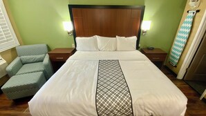 Hotellihuone, jossa on sänky, kaksi yöpöytää, tuoli ja seinälle kiinnitetty silityslauta.