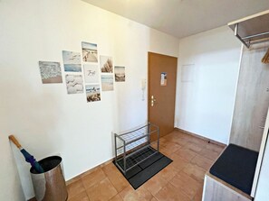 Un couloir avec une porte, un étagère en métal et une poubelle.
