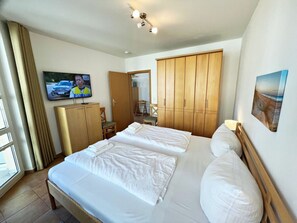 A hotel room with two beds, a television, a wardrobe, and a painting on the wall. - Apartment Building Linquenda 10 (Heringsdorf)