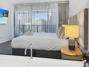 Ein modernes Hotelzimmer mit einem großen Bett, einem Nachttisch mit Lampe und Blick auf die Stadt durch transparente Vorhänge.