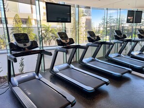 Ein Fitnessraum mit mehreren Laufbändern, einem Ergometer und einem an der Wand befestigten Fernseher.