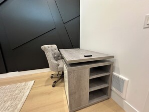 A corner room with a grey upholstered chair, a grey table with a remote, and a white wall with a black geometric design. - Modern Bremerton Escape Near Ferry & Seattle (Bremerton)