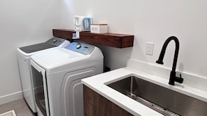 A laundry area with a washing machine, a sink, and a shelf with a box labeled 'DRYER SHEETS.' - Modern Bremerton Escape Near Ferry & Seattle (Bremerton)