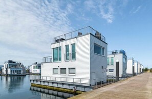 Ein modernes Gebäude am Wasser mit flachem Dach, großen Fenstern und einer Holzterrasse.