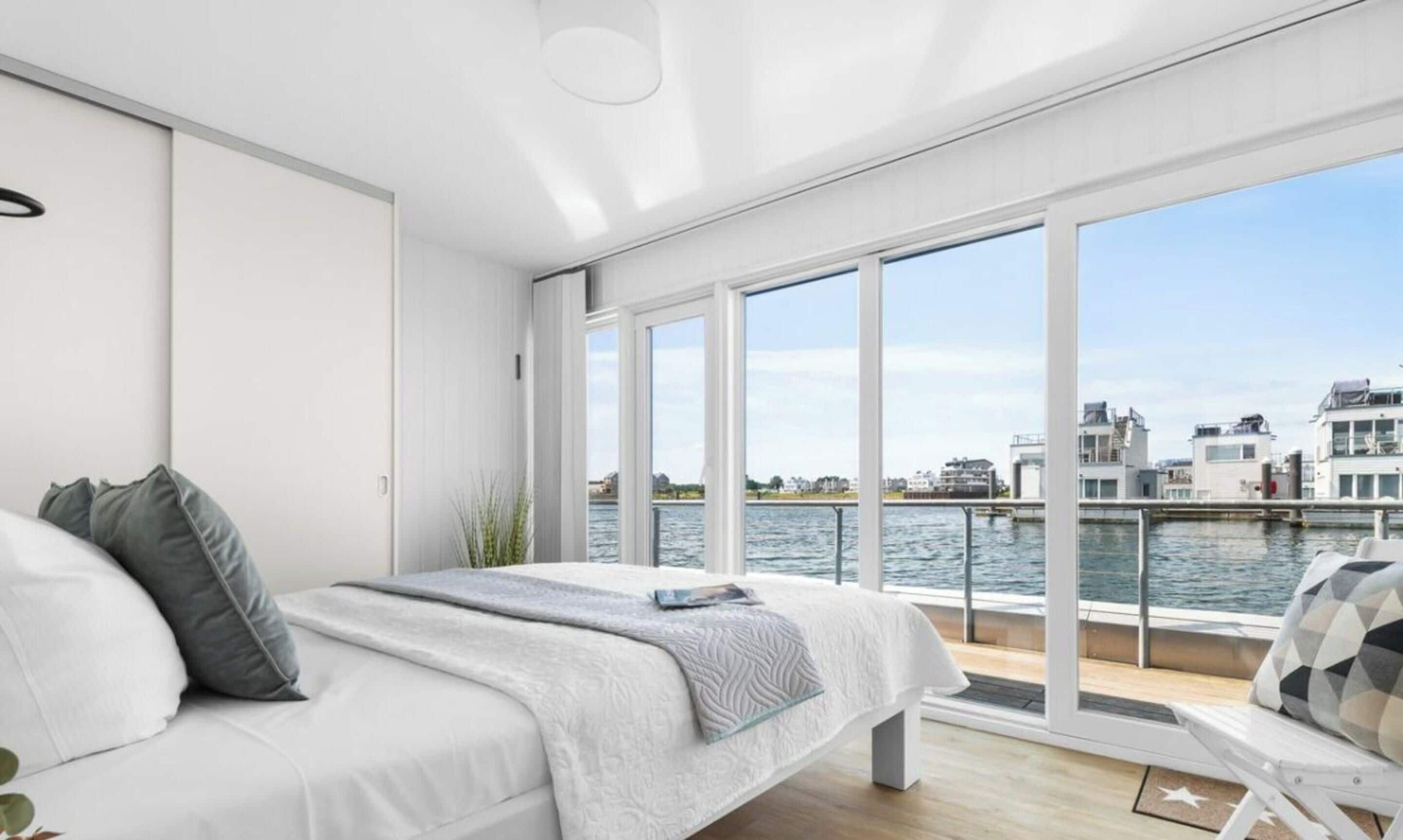 Une chambre moderne dotée d’une grande fenêtre donnant sur un plan d’eau et des bâtiments.