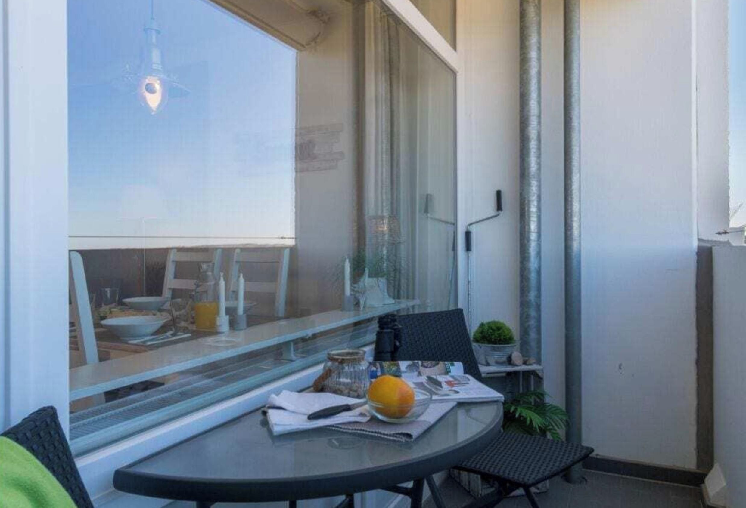 Un pequeño balcón con una mesa, una silla, una planta en maceta y una ventana con vista a la ciudad.