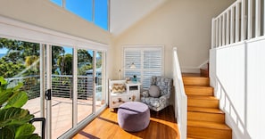 A modern interior with a staircase, a seating area with a patterned sofa, and a view through large glass doors. - Carinya Coastal Escapes | Bay Views & Bouddi (Daleys Point)