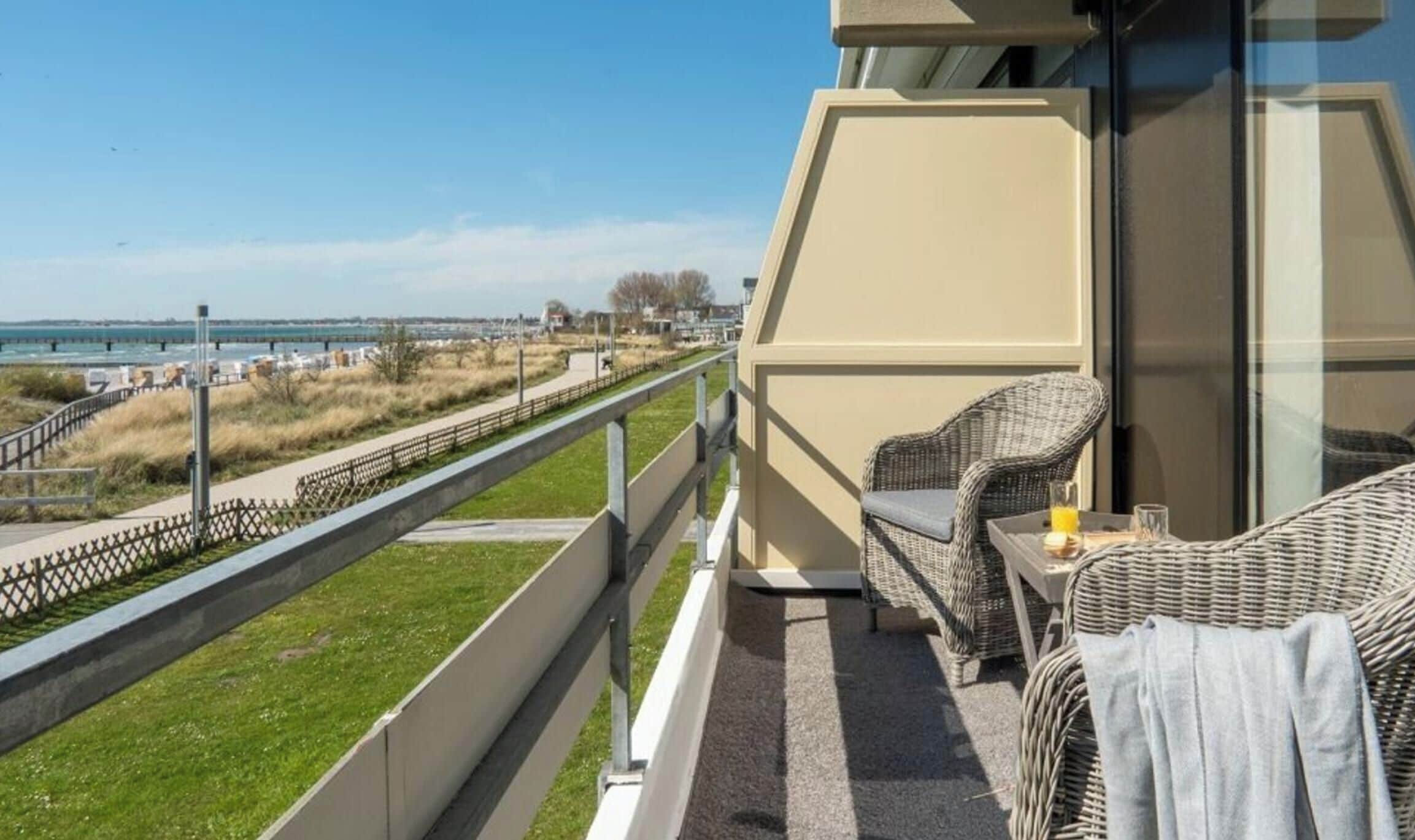 A balcony with wicker furniture, a glass table, and a view of the sea and a bridge.