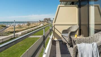 A balcony with wicker furniture, a glass table, and a view of the sea and a bridge.