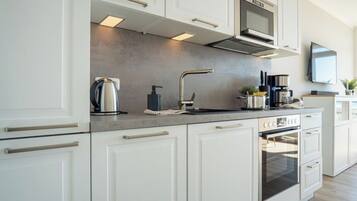 A modern kitchen with white cabinetry, stainless steel appliances, and a built-in oven.