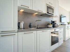 A modern kitchen with white cabinetry, stainless steel appliances, and a built-in oven. - Bellevue, House A, Apartment 19 (Grossenbrode)