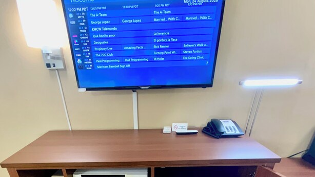 Une chambre d’hôtel équipée d’un téléviseur affichant un programme, d’un bureau avec un téléphone et d’un mini-réfrigérateur intégré.