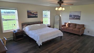 Une chambre à coucher avec un lit, un canapé en cuir marron, un ventilateur de plafond et de grandes fenêtres.