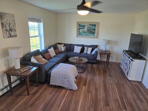 A living room with a sectional sofa, a coffee table, a TV stand, and a painting on the wall.