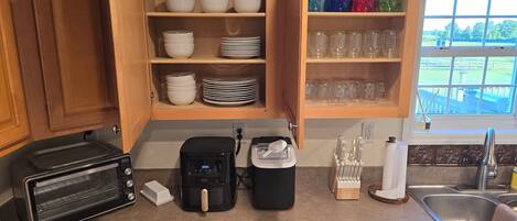 A kitchen with wooden cabinets, a toaster oven, a coffee maker, and a window with a view of a yard.