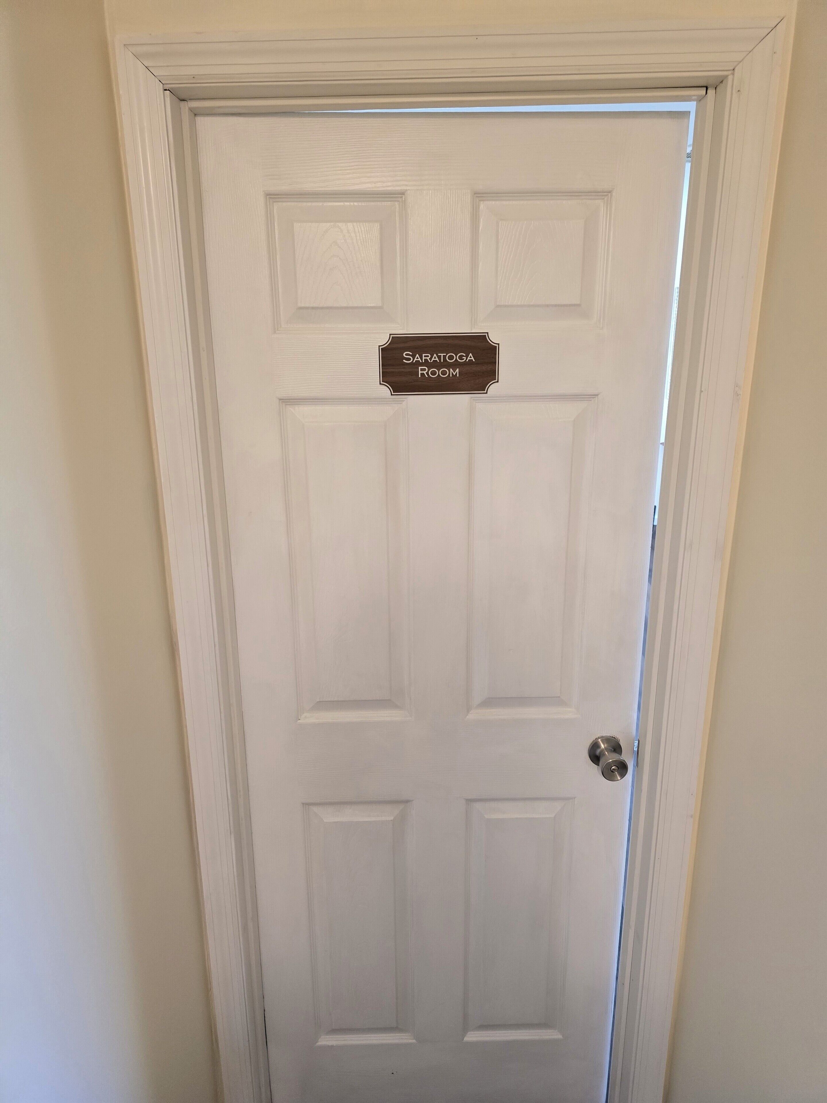 Une porte blanche avec une plaque indiquant « Salle Saratoga » et un trou de serrure.