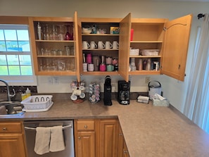 A kitchen with open wooden cabinets, a coffee maker, and various kitchenware.