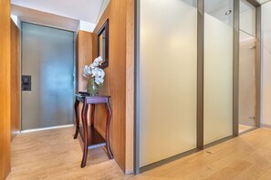 Un pasillo con puerta de madera, pared de vidrio y una pequeña mesa con un florero.