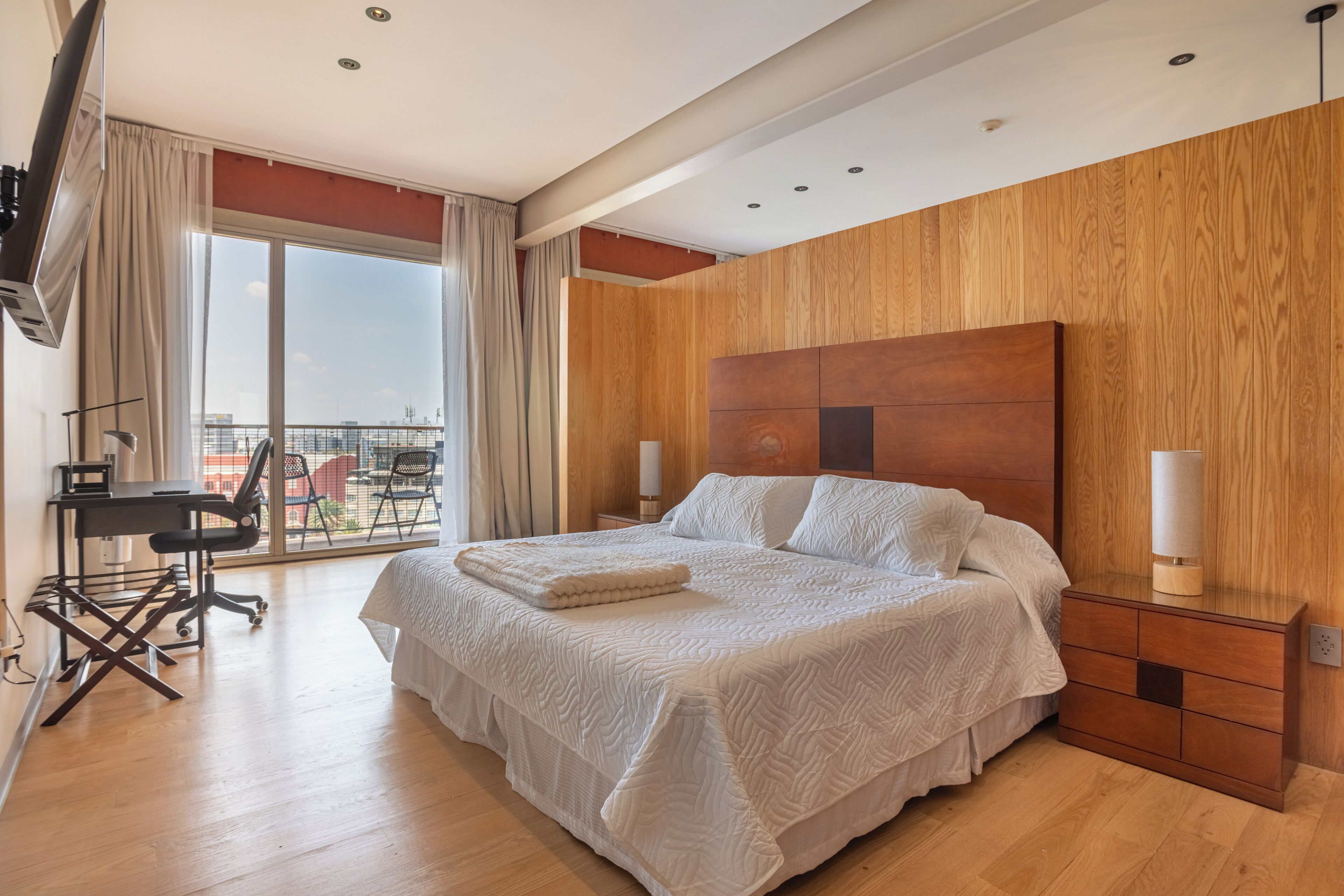 A hotel room with a large bed, a desk, and a view of the city.