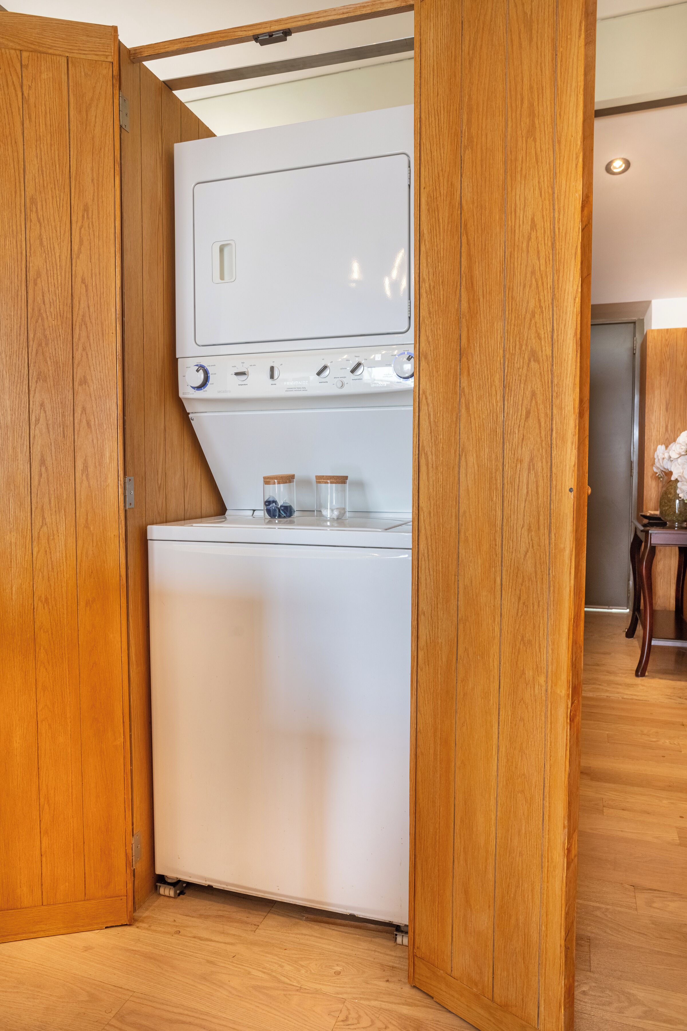Une petite buanderie comprenant un lave-linge et un sèche-linge, des armoires en bois et une petite table avec des bocaux.