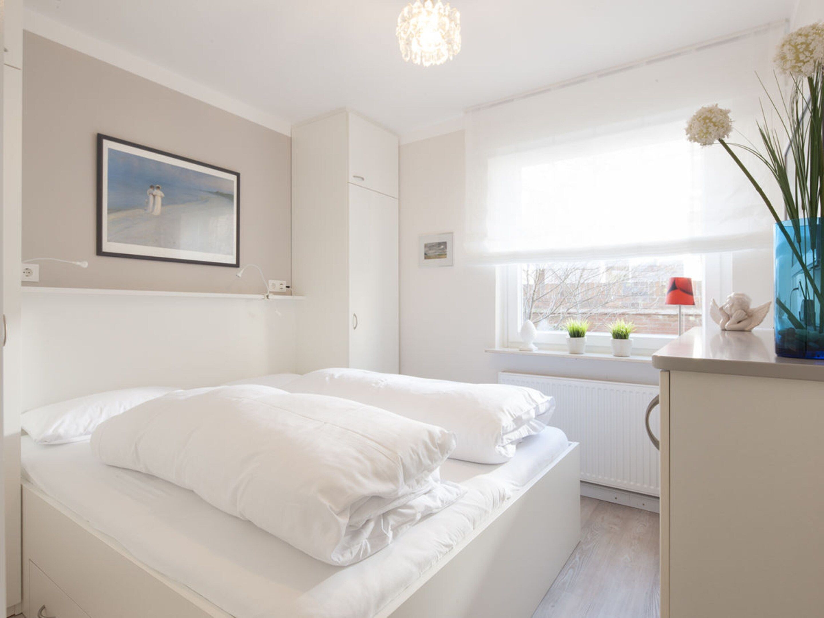 A bedroom with a bed, a window with a view, a radiator, and a vase with flowers.