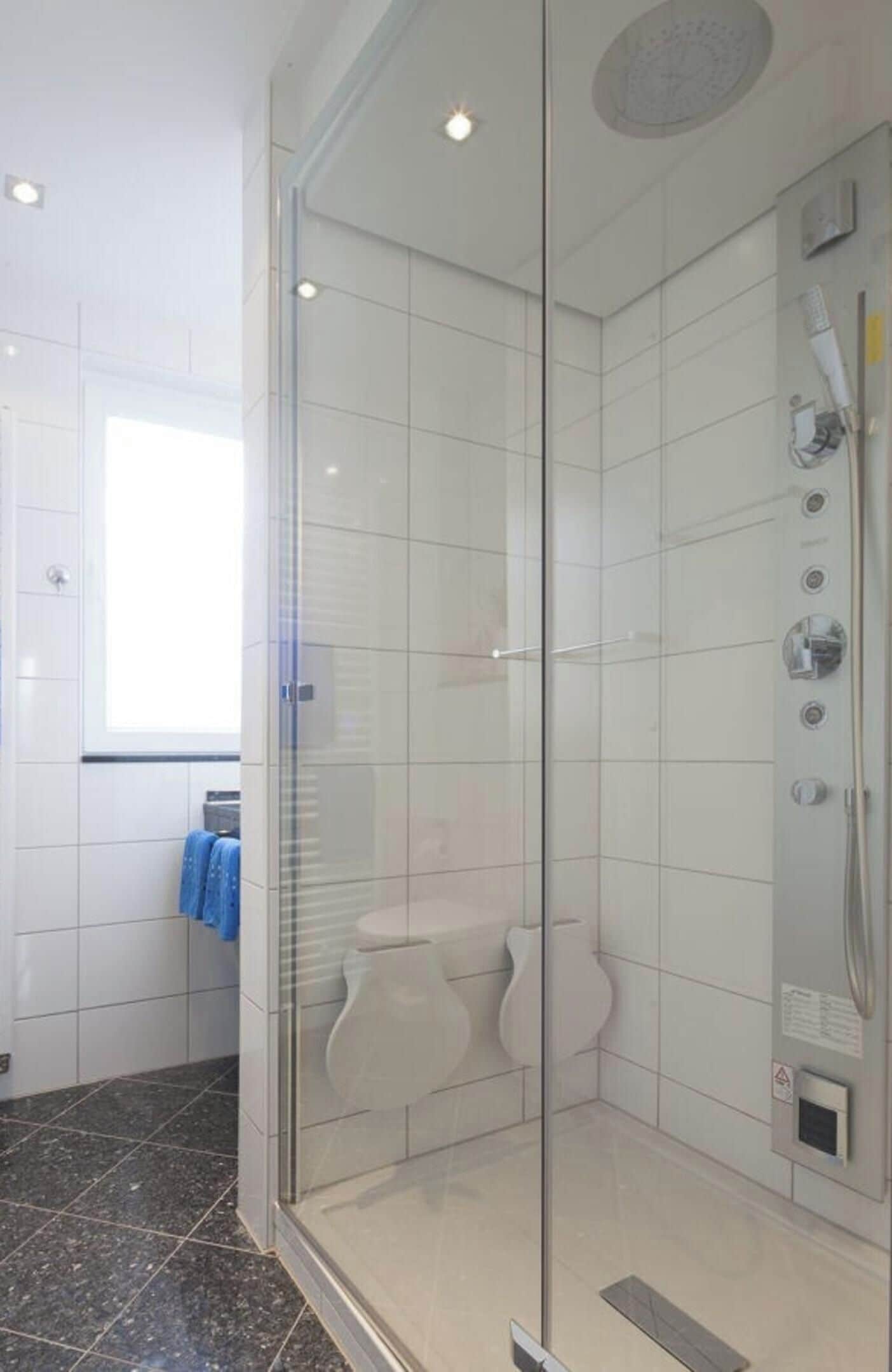 Et moderne badeværelse med en glasvæg omkring brusenichen, hvide fliser og et fritstående toilet.