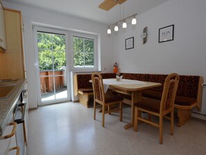 Un comedor con una mesa y sillas, un banco, una cocina con estufa y vistas por una puerta de cristal.