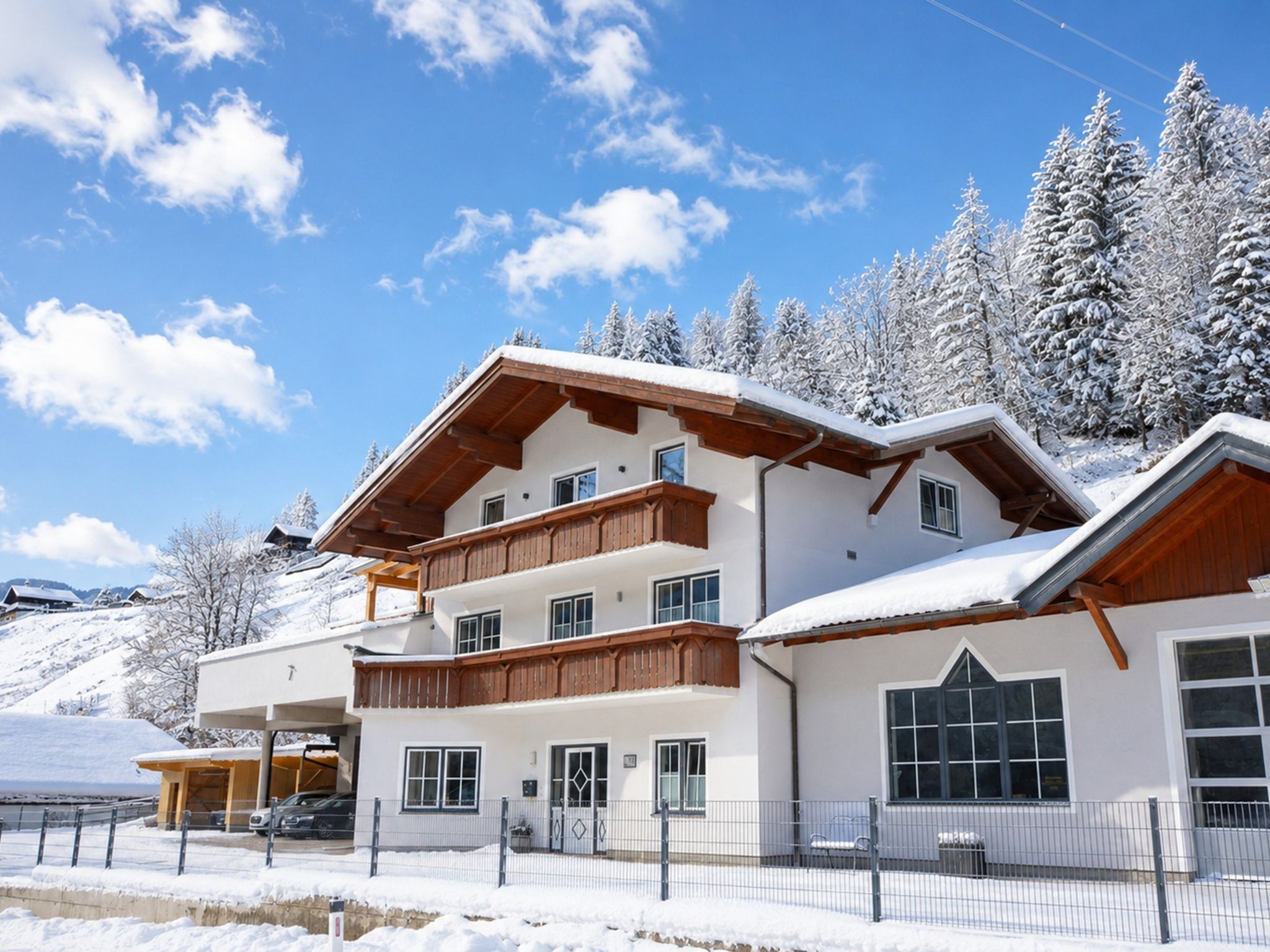Un hôtel à plusieurs étages doté de balcons, avec une piste de ski en arrière-plan et des arbres couverts de neige.