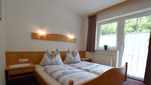 Quarto com cama de madeira, duas mesas de cabeceira, janela com cortinas e luminárias fixadas na parede.